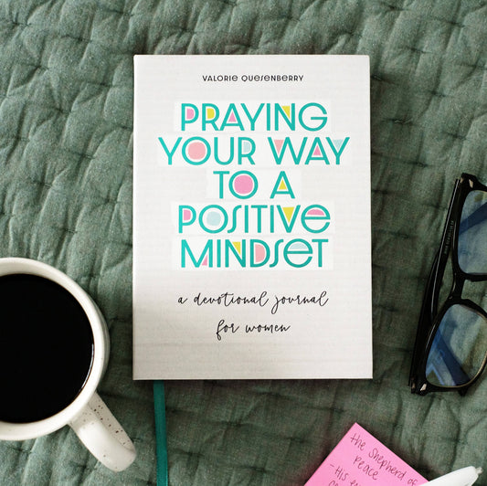 Book titled 'Praying Your Way to a Positive Mindset' on a textured surface with a cup of coffee and glasses.