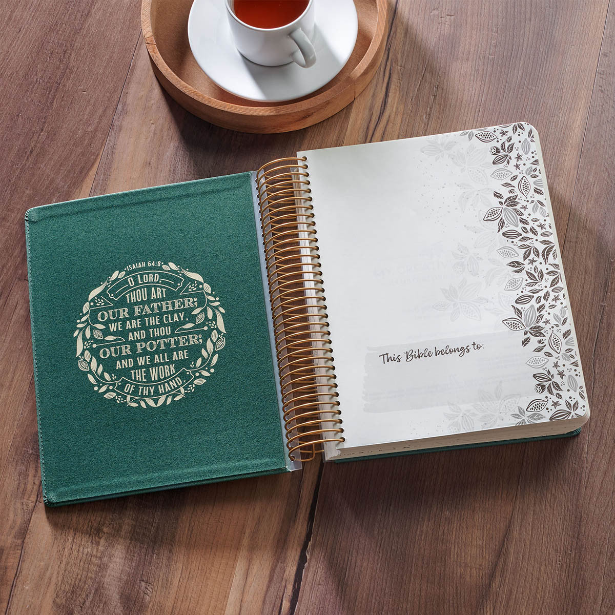 Open Bible with green cover on a wooden surface, next to a cup of tea.