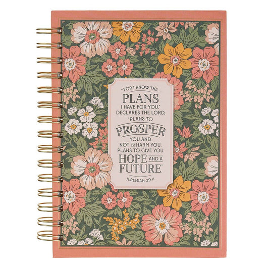 A spiral-bound planner with a coral pink border and a floral patterned cover featuring pink, yellow, and white flowers on a green background. A central cream label displays a Bible verse from Jeremiah 29:11.